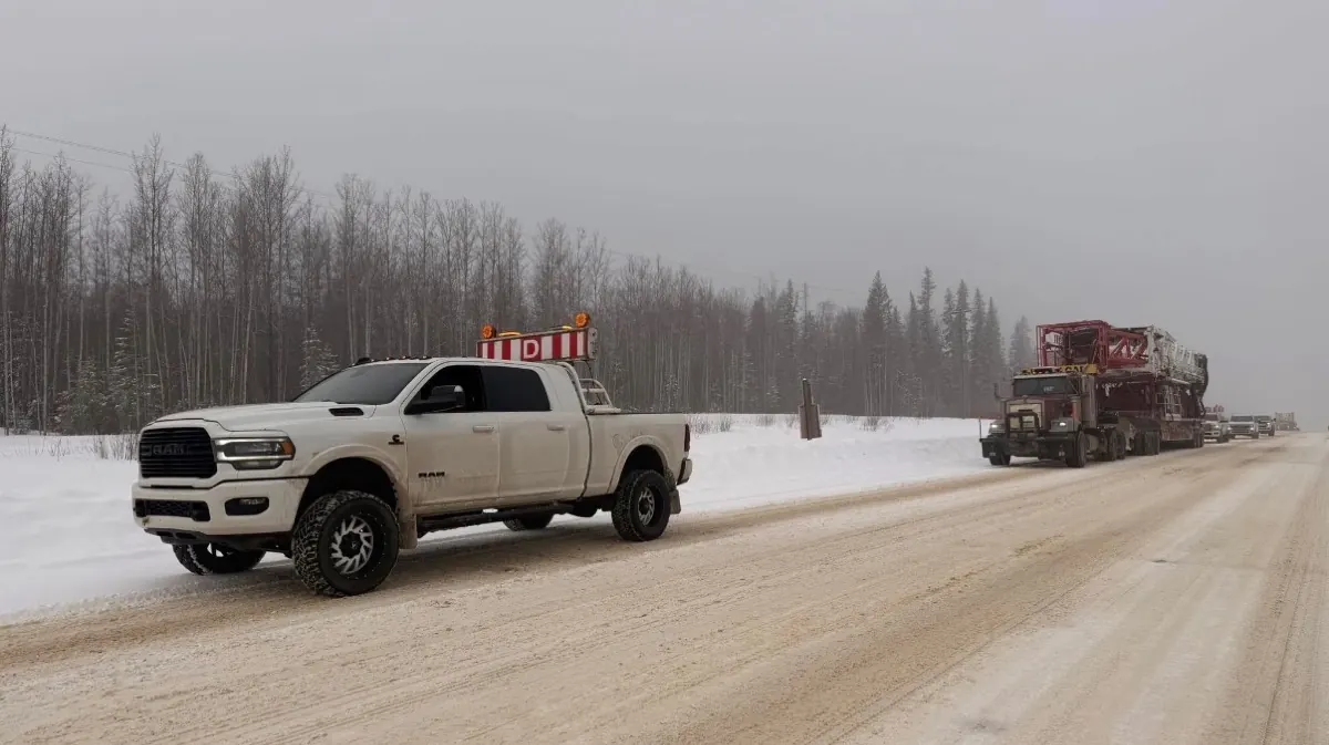 Rig Dawgs pilot truck with the sign board up, oversized load behind it on a snowy Alberta highway